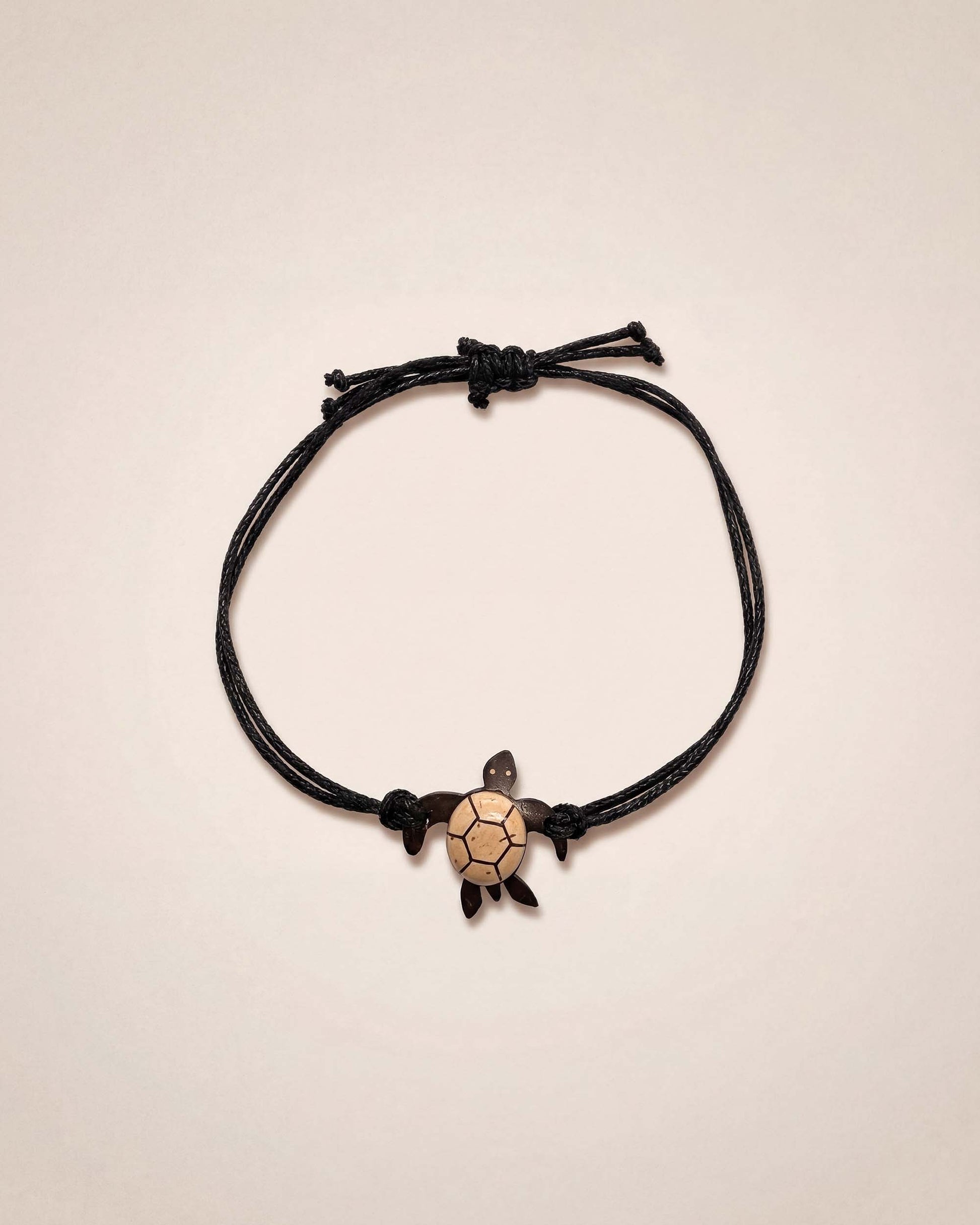 Black cord bracelet with a turtle charm on a beige background