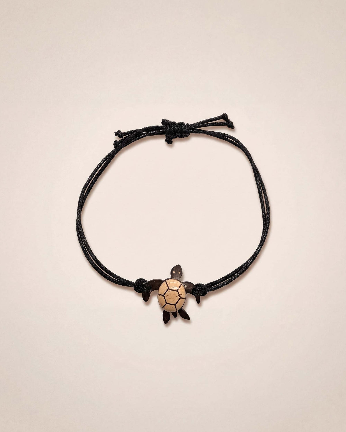 Black cord bracelet with a turtle charm on a beige background