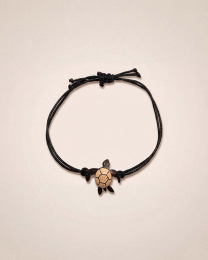 Black cord bracelet with a turtle charm on a beige background
