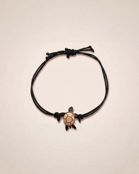 Black cord bracelet with a turtle charm on a beige background