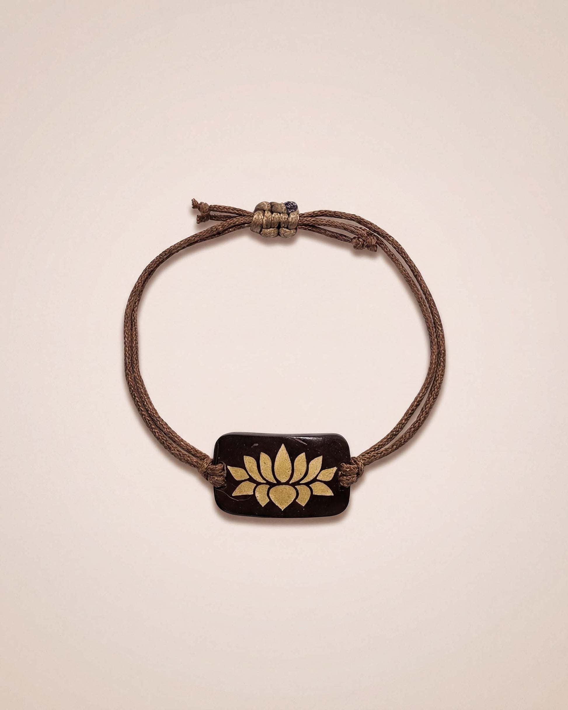 Bracelet with a brown cord and gold emblem on a beige background