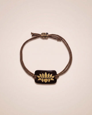Bracelet with a brown cord and gold emblem on a beige background