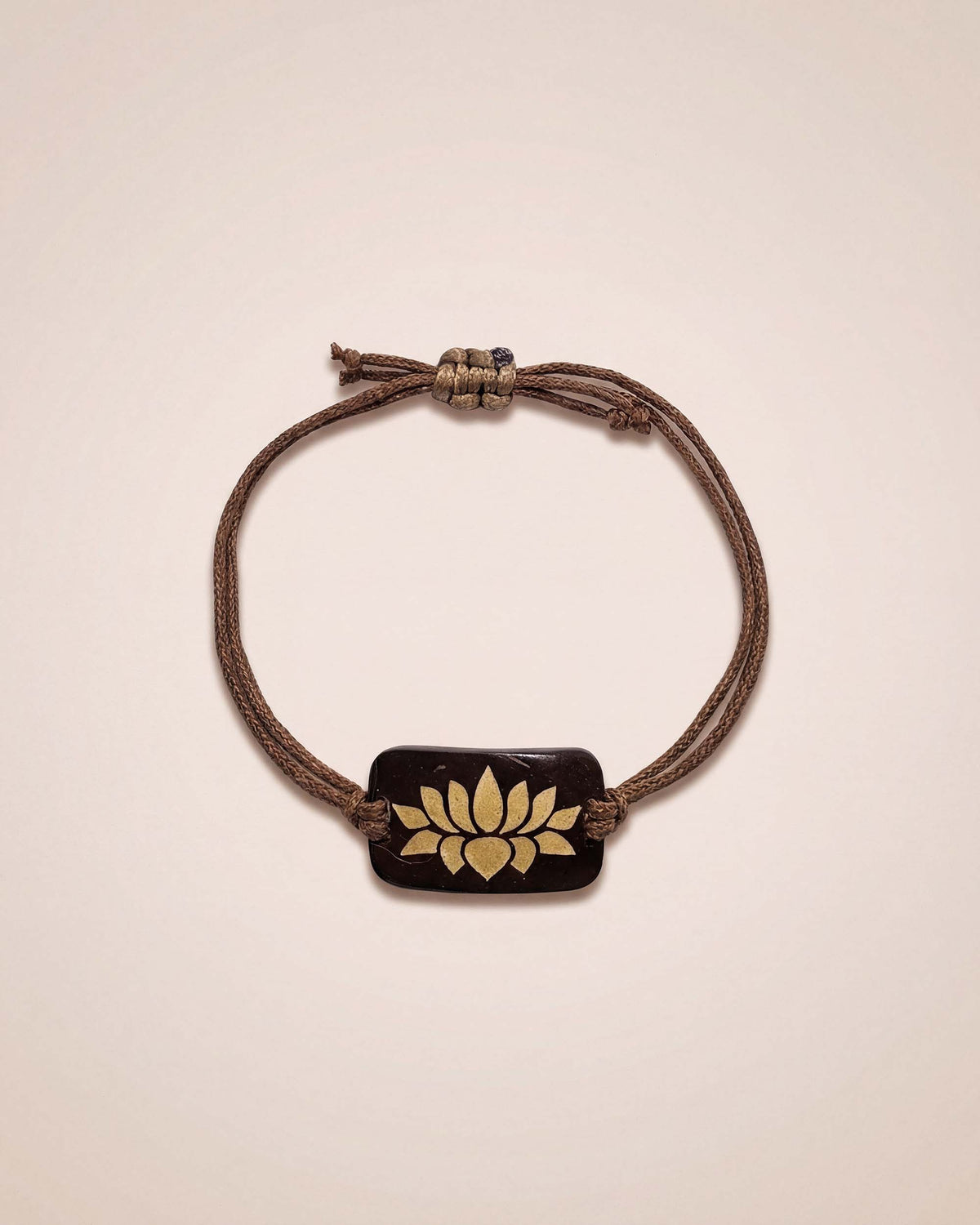 Bracelet with a brown cord and gold emblem on a beige background