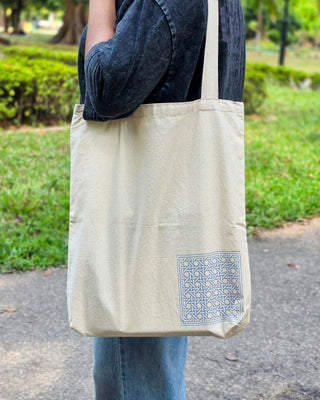 Person holding a beige tote bag with a geometric pattern in an outdoor setting